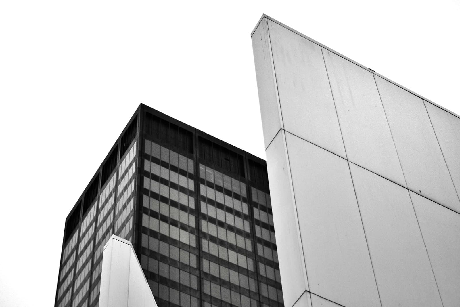 A dark glass tower beside a light concrete wall, in black and white
