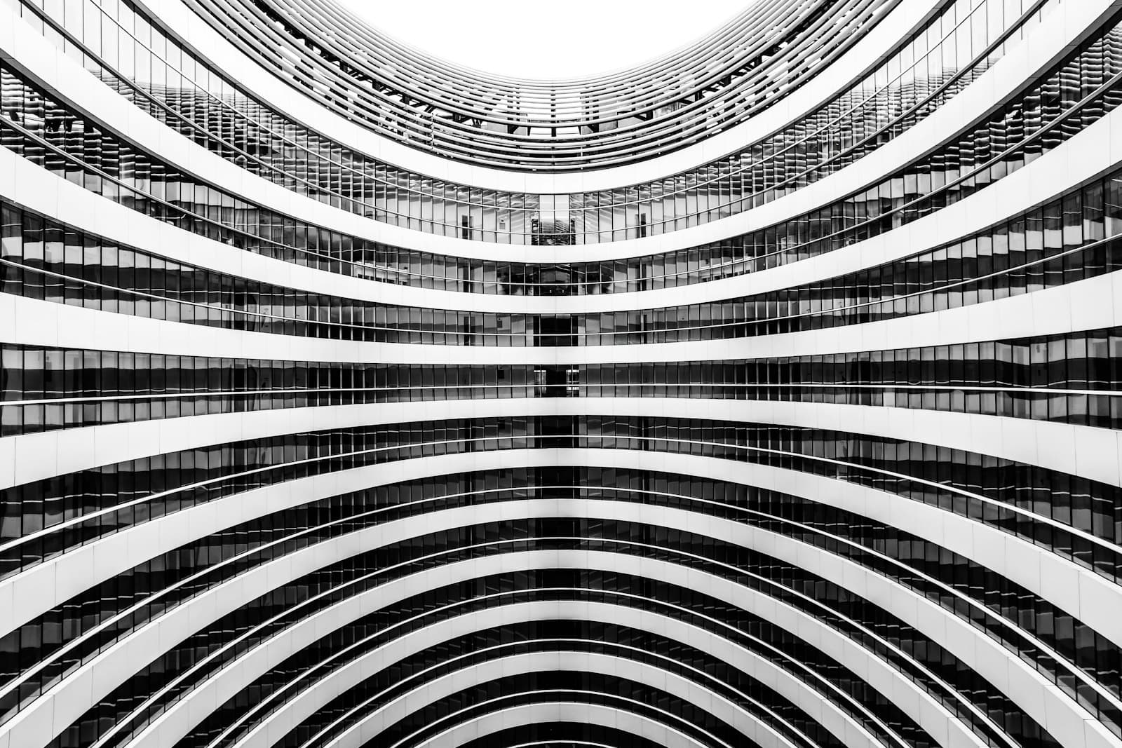 Curved balconies repeating around an atrium, seen from below, in black and white