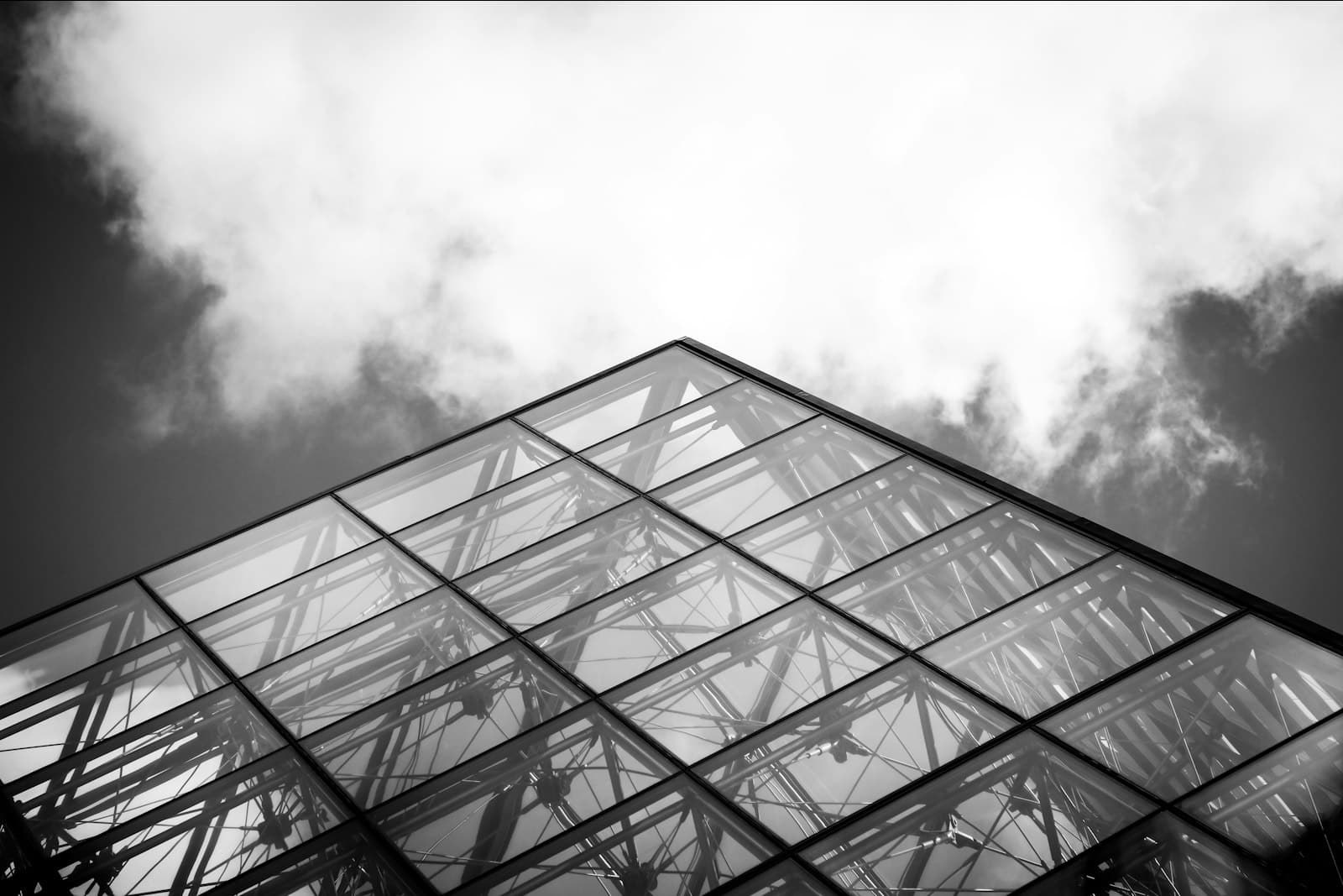 Glass roof structure seen from below against a cloudy sky, in black and white